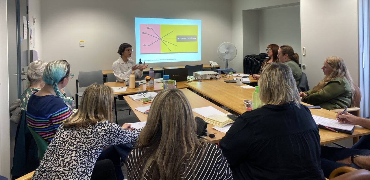 Sara speaking to a group of people with a presentation behind